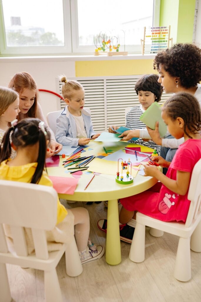 A teacher sits at a table with learners who are engaged in an exciting activity.